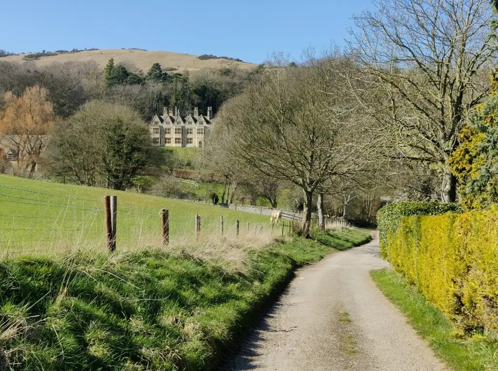 Cotswold Way path leading towards Postlip Hall through rolling Cotswold farmland